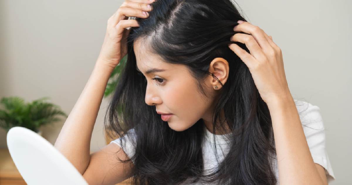 Woman examining thinning hairline in mirror, showing early signs of hair loss and need for hair restoration treatment in Red Bank, NJ.